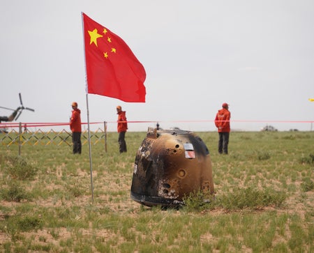 China’s Chang’e 6 sample-return capsule surrounded by three people in red jackets and a Chinese flag