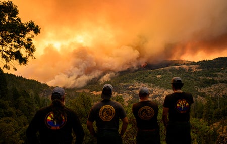 Firefighters watch as flames and smoke move through a valley.