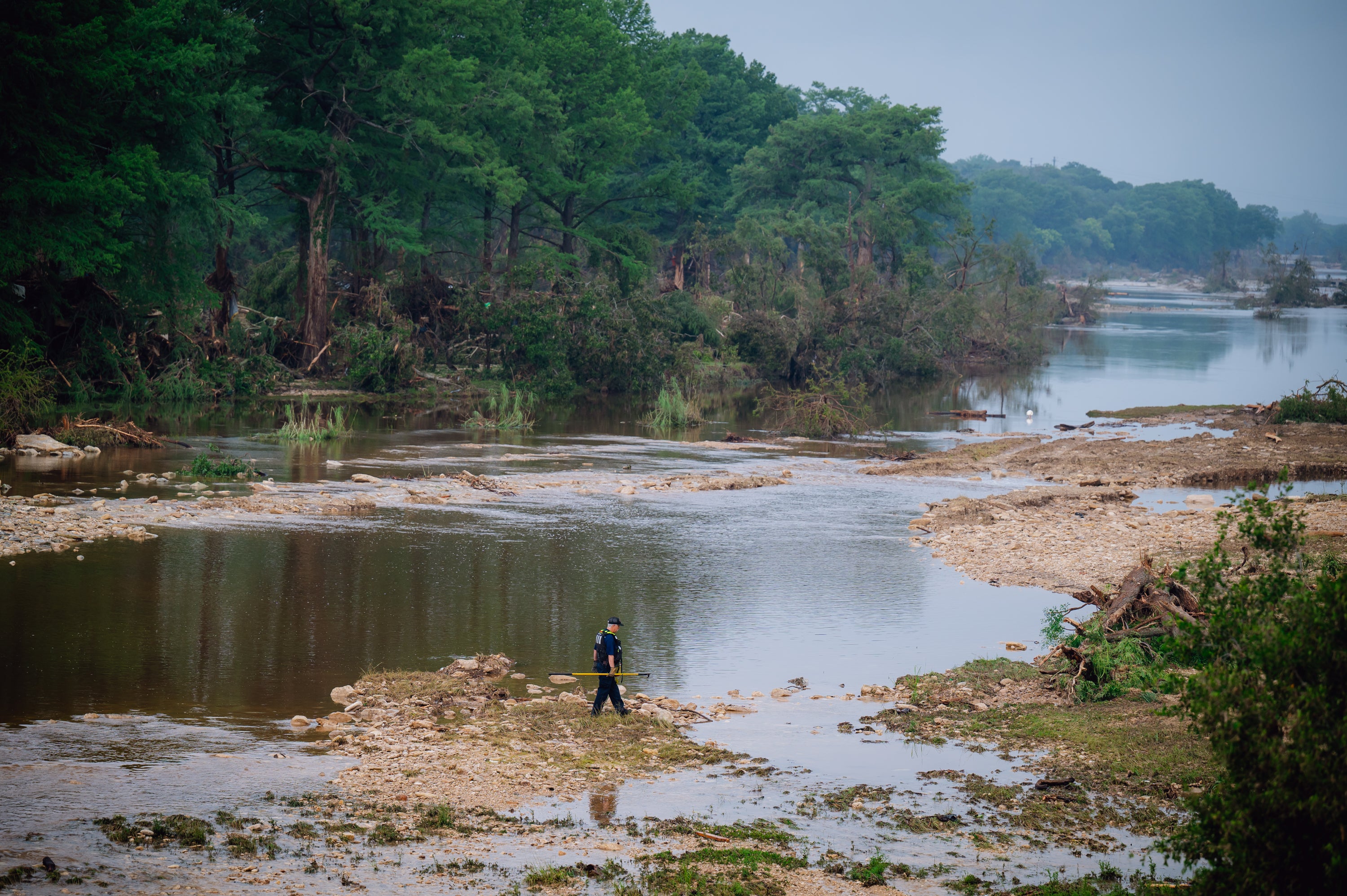 Man in vest walks through muddy field near river