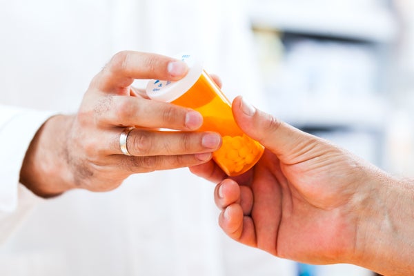 a close up of a pharmacist handing a bottle of pills to a customer