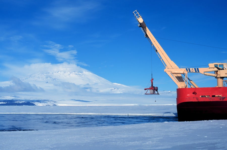 Red icebreaker ship with blue crane mounted on deck.