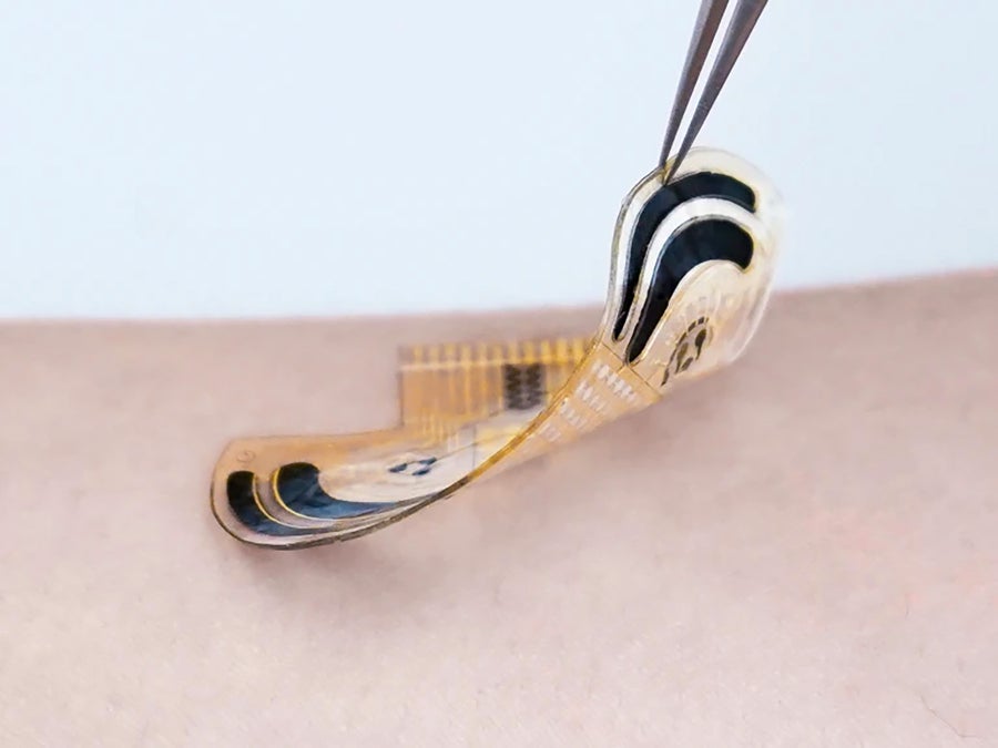A close-up of tweezers lifting a wafer-thin stress sensor from someone’s skin