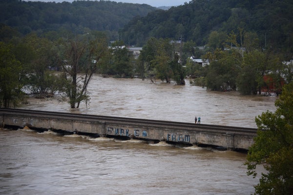 Two people walk on bridge over flooded river