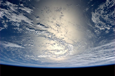 Sunlight reflects off the surface of the Earth against clouds.