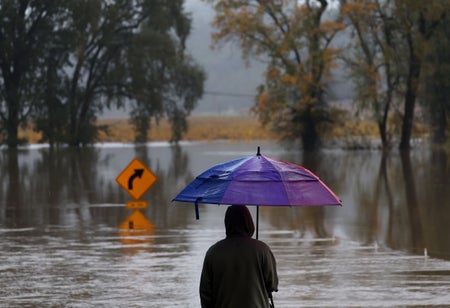 A resident with purple umbrella looks over a flooded road