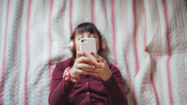 Teenager in bed is listening to music with a phone