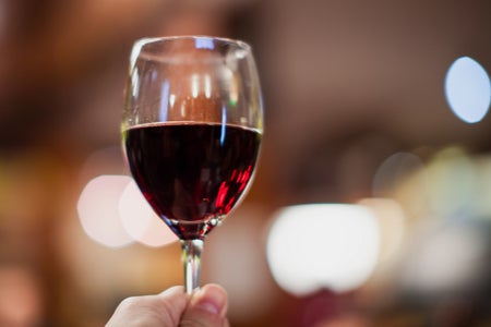 hand holding glass of red wine with festive lights background.