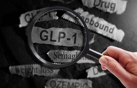 GLP-1 related drugs newspaper headlines with hand and magnifying glass.