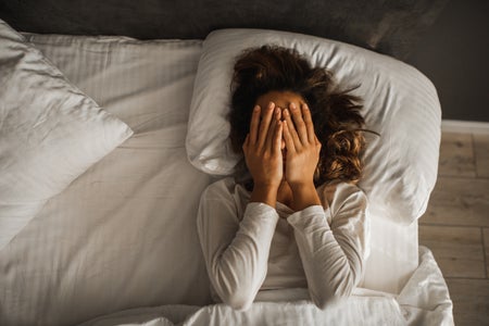 woman covering face with her hands who can't sleep in bed