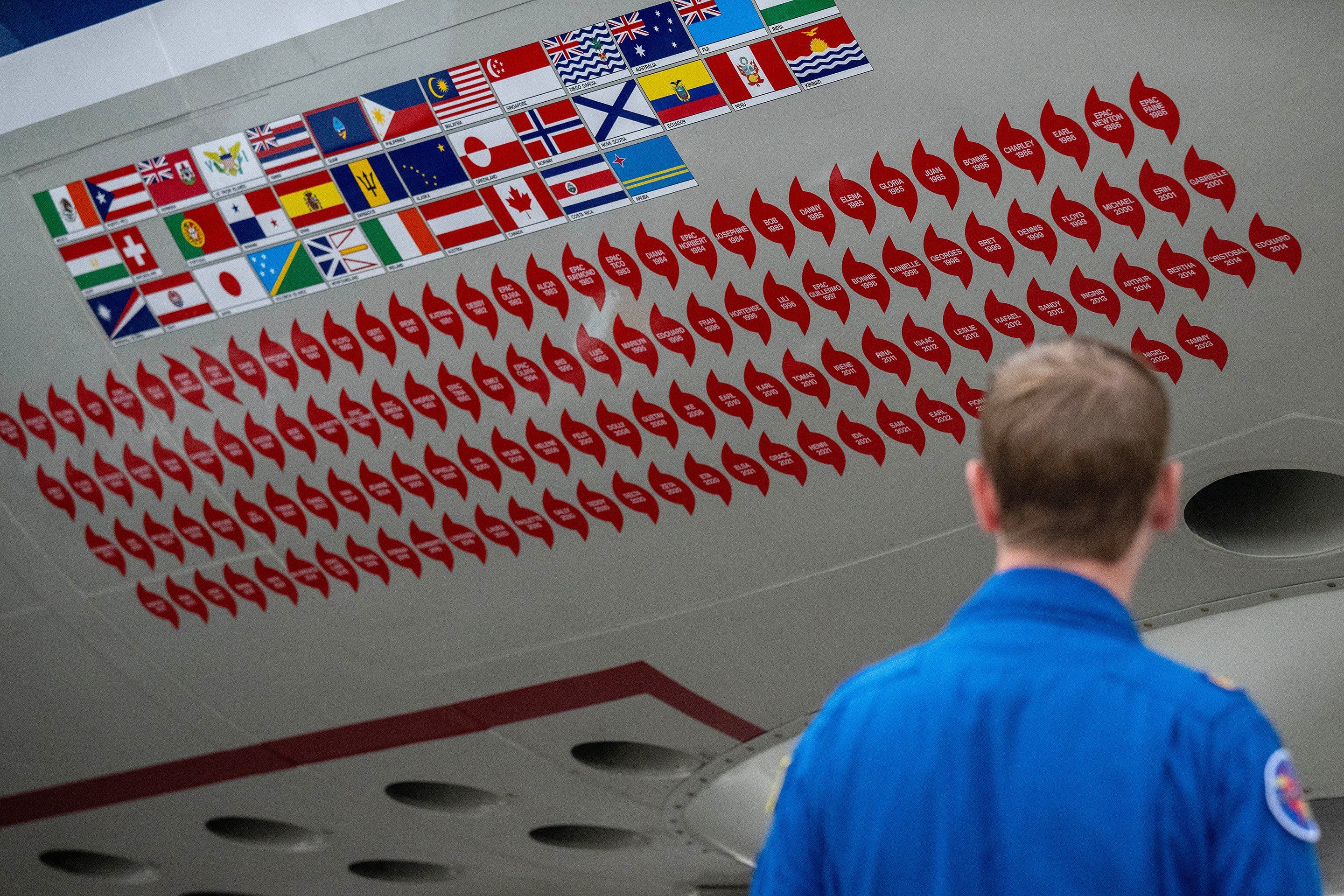 Close up view of stickers from previous hurricane missions adorn the side as a crew member walks past "Kermit", a National Oceanic and Atmospheric Administration (NOAA) WP-3D Orion hurricane hunter aircraft