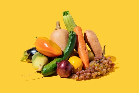 Carrot, grapes, squash, and other vegetables arranged on a yellow background