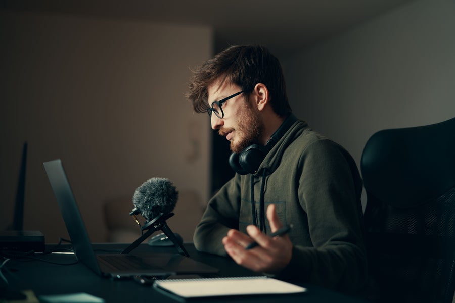 Side view of a young bearded person speaking into a microphone at a laptop