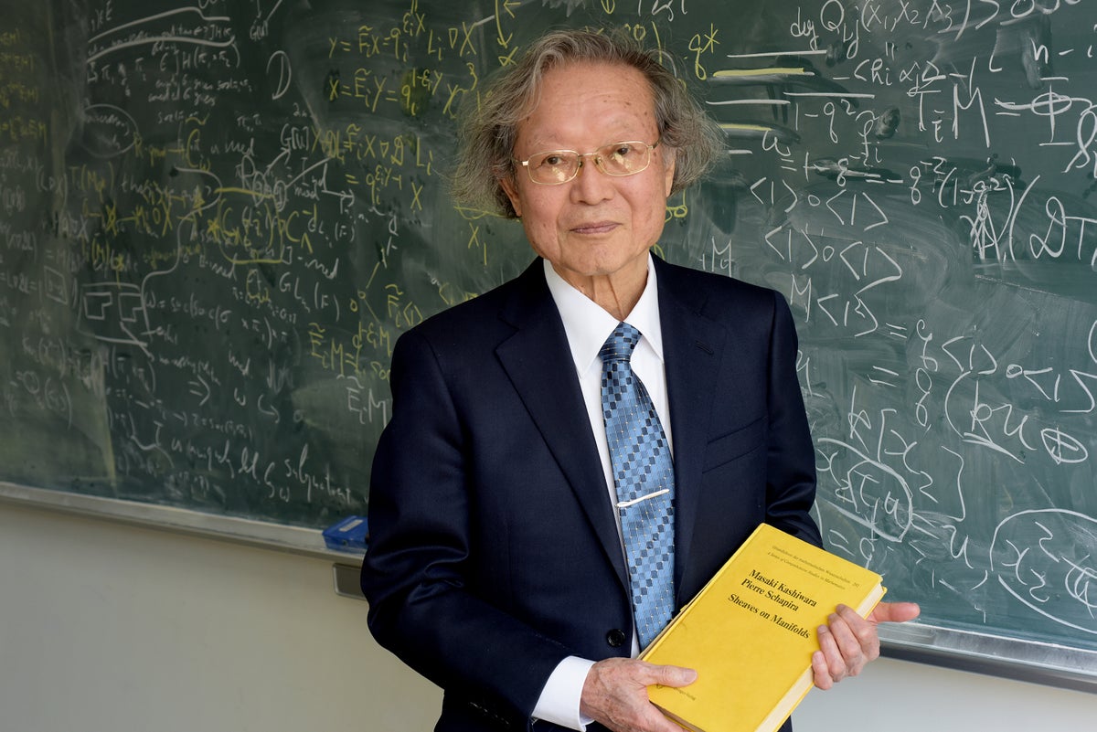 Portrait of Masaki Kashiwara, Abel Prize Laureate 2025, in front of a chalkboard and holding his book titled Sheaves on Manifolds