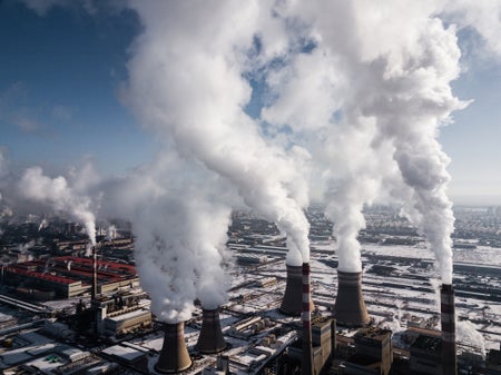 White steam and smoke rises from smokestacks against a blue sky