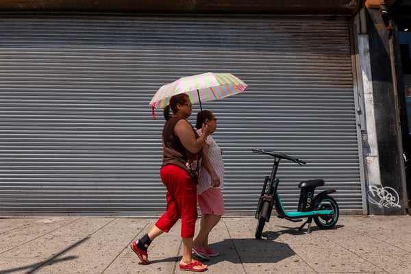 Two women walking on sidewalk holding umbrellas on a sunny day.