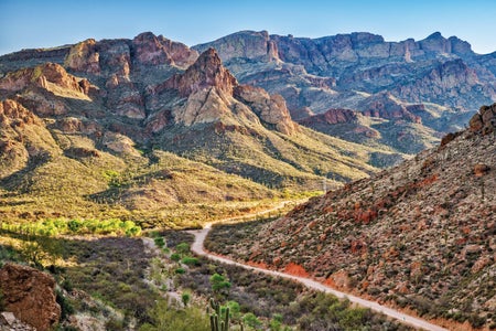 View east in Tonto National Forest from Fish Creek Hill vicinity, over the Apache trail and a valley, with dramatic rocky features peppered with cacti and other vegetation.