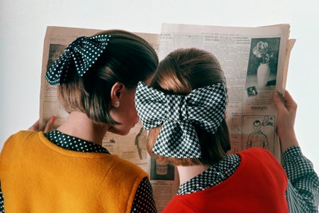 Two women with bows in their hair seen from behind in a photograph from the 1960s.