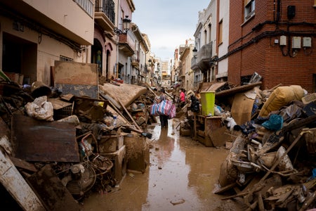 People walk a debris-lined flooded street
