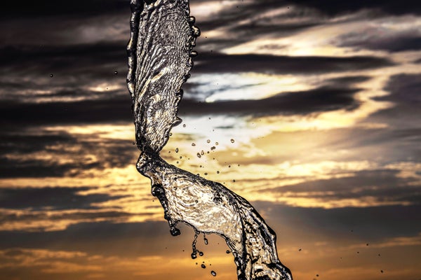 High-speed photo of a stream of water twisting as it is thrown with a cloudy, warm colored sky in the background