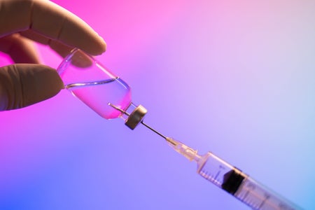 Syringe and coronavirus vaccine against a pink and purple background