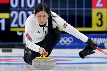 A woman crouches down in preparation to throw a curling rock