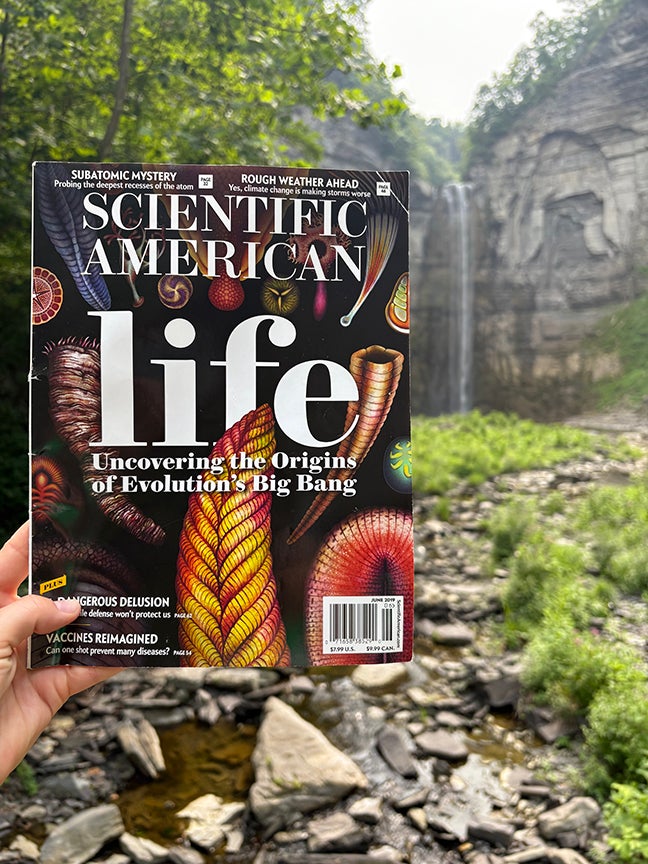 Person holding Scientific American Magazine in front of waterfall