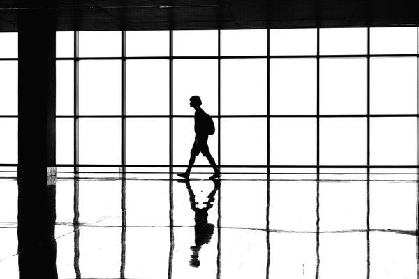 Person with a backpack walking across reflective floor with multi paneled windows in the background