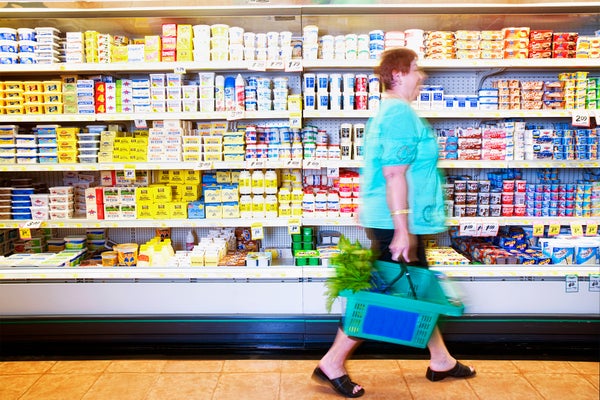 Hispanic woman carrying shopping basket passing in front of a dairy cooler in grocery store