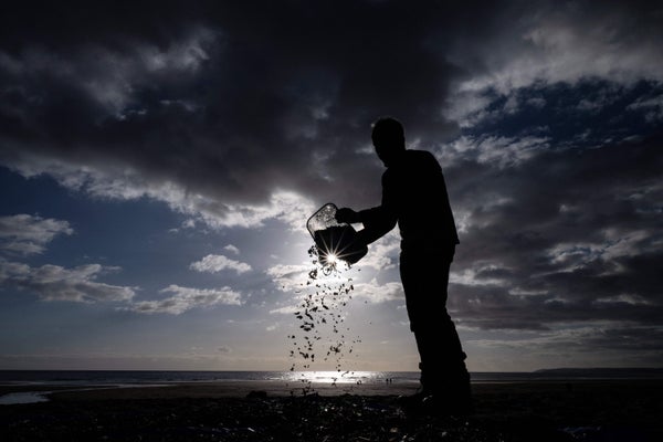 A figure pours microplastics and nurdles out onto a tarp at the beach during cleanup