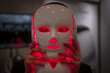 A person holds a glowing red light mask in front of their face