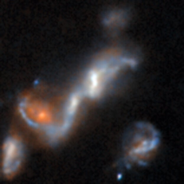 A small image of several galaxies with distorted shapes. The central galaxy is bluish in colour with a bright center. It is stretched out into a long, curled bar. At one end sits a reddish galaxy, which the bar curves around.