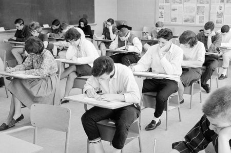 Black-and-white photograph of a room full of teenage students bent over their desks taking an exam.