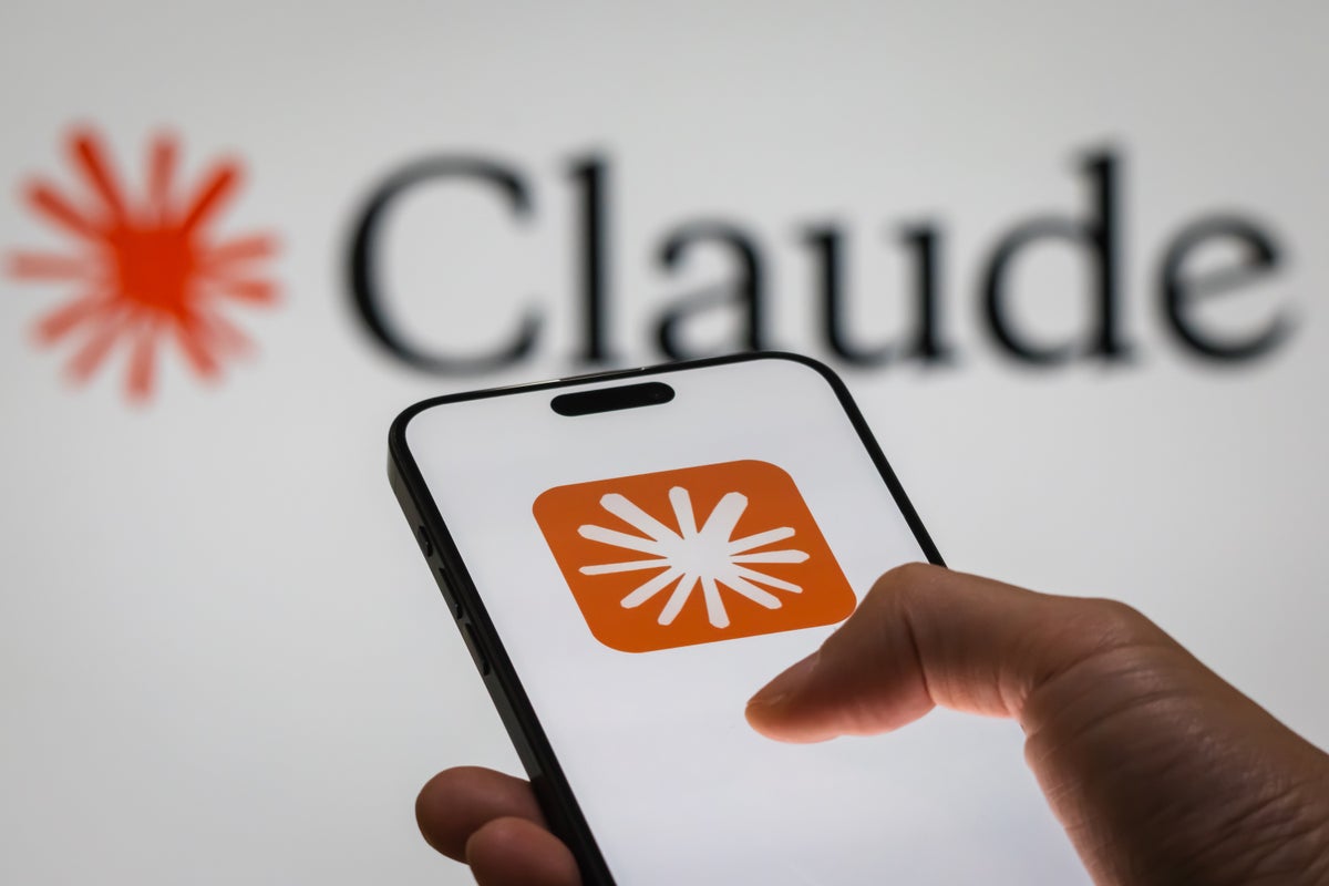 A hand holding a smartphone that displays the Claude app logo on the screen, with the Claude brand name blurred in the background.