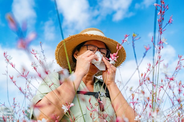Older woman having an allergic reaction to pollen with flowers in the foreground