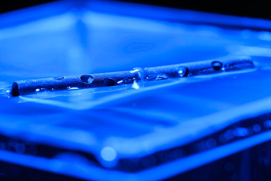 कई ड्रिल किए गए छेदों वाली एक लंबी धातु ट्यूब नीले रंग के आसुत जल की सतह पर तैरती है।