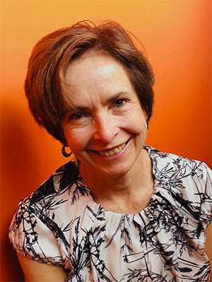 A smiling Sue Smrekar against an orange background.