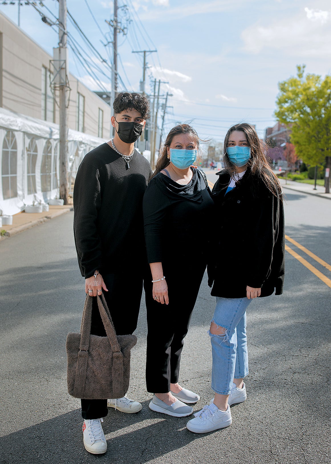 Three people wearing face masks and black clothing posing together on the street.