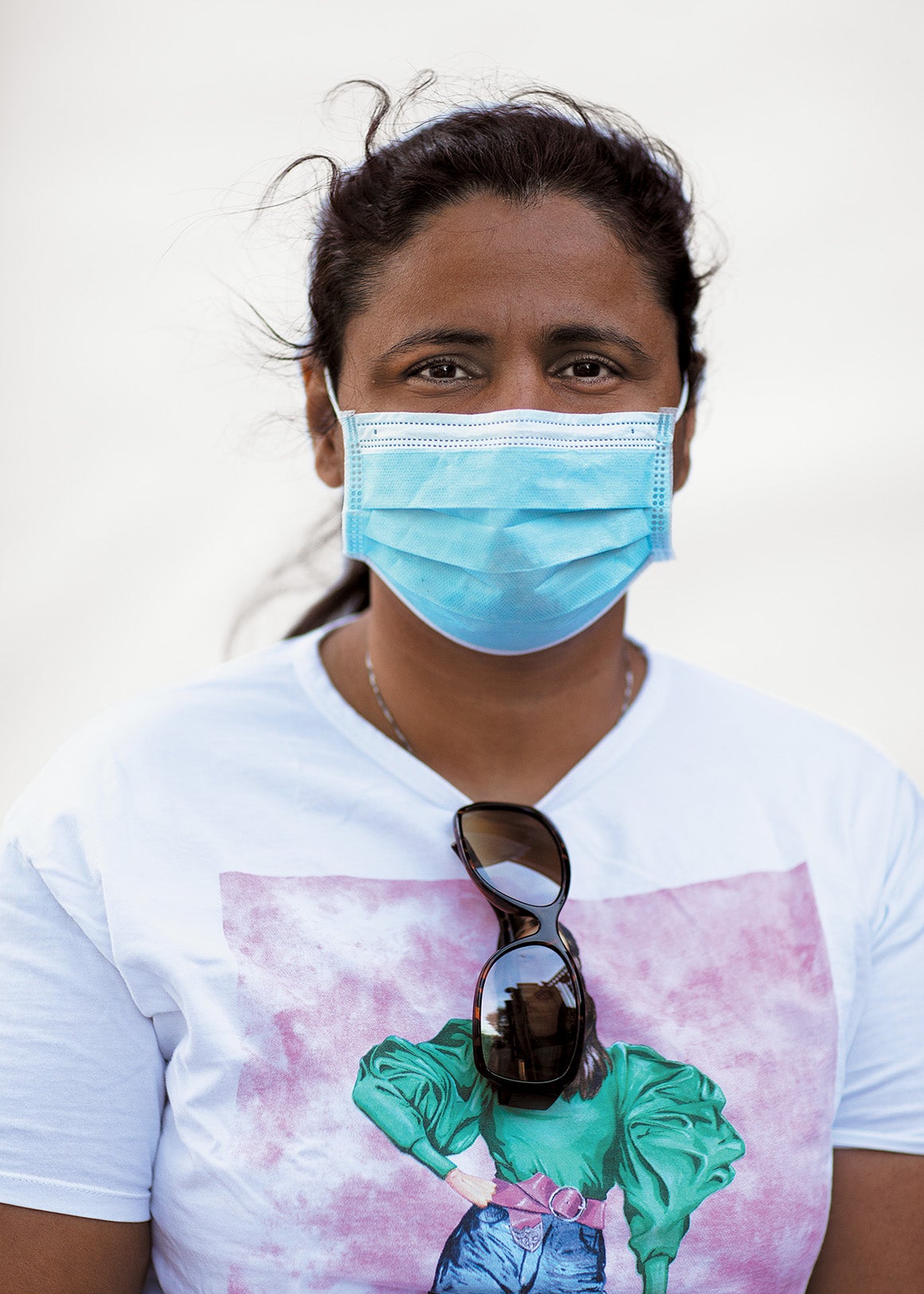 Kajal Negandhi wearing a face mask standing against white background.