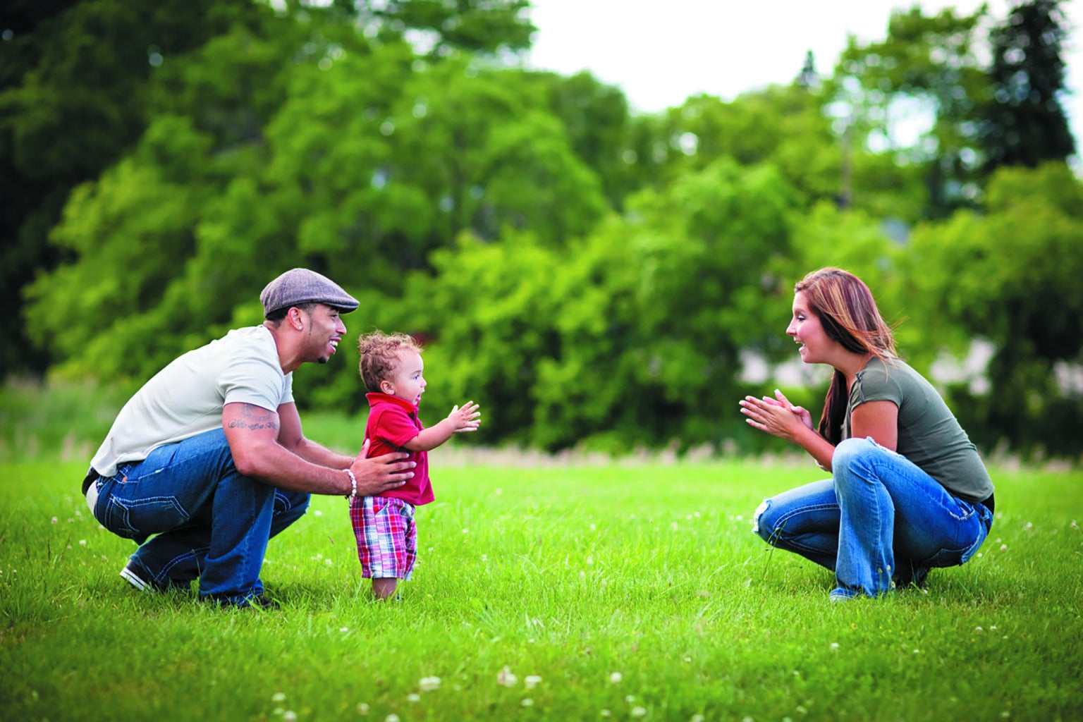 Parents encouraging toddler to walk at a park.