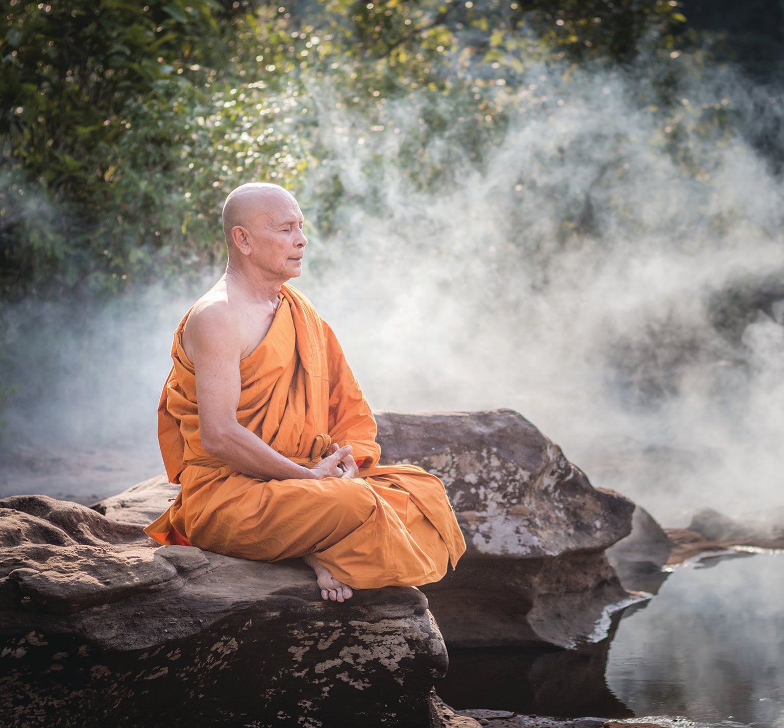 Monk meditating while sitting on a rock.