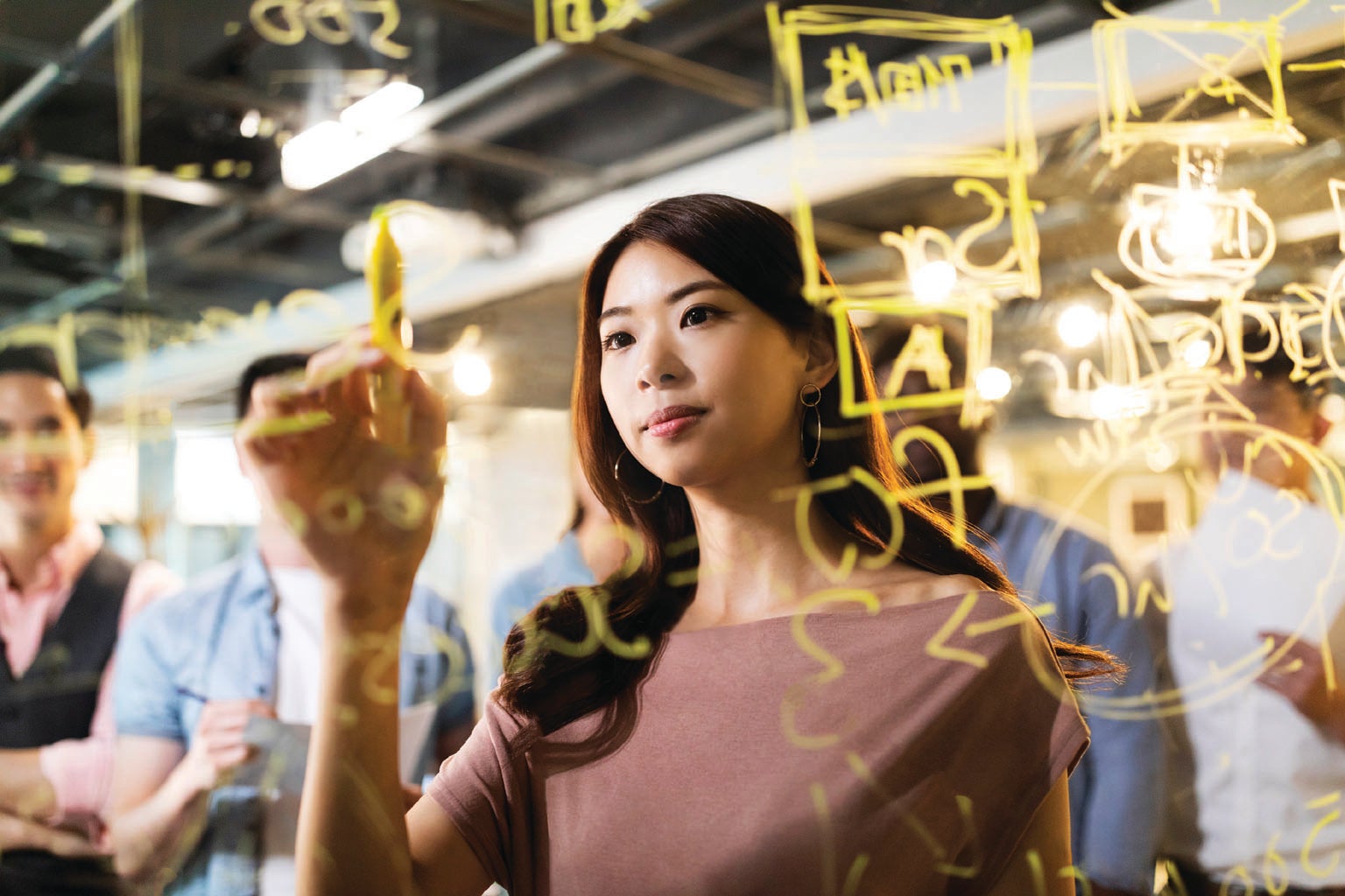 Woman writing on a clear board surrounded by colleagues.