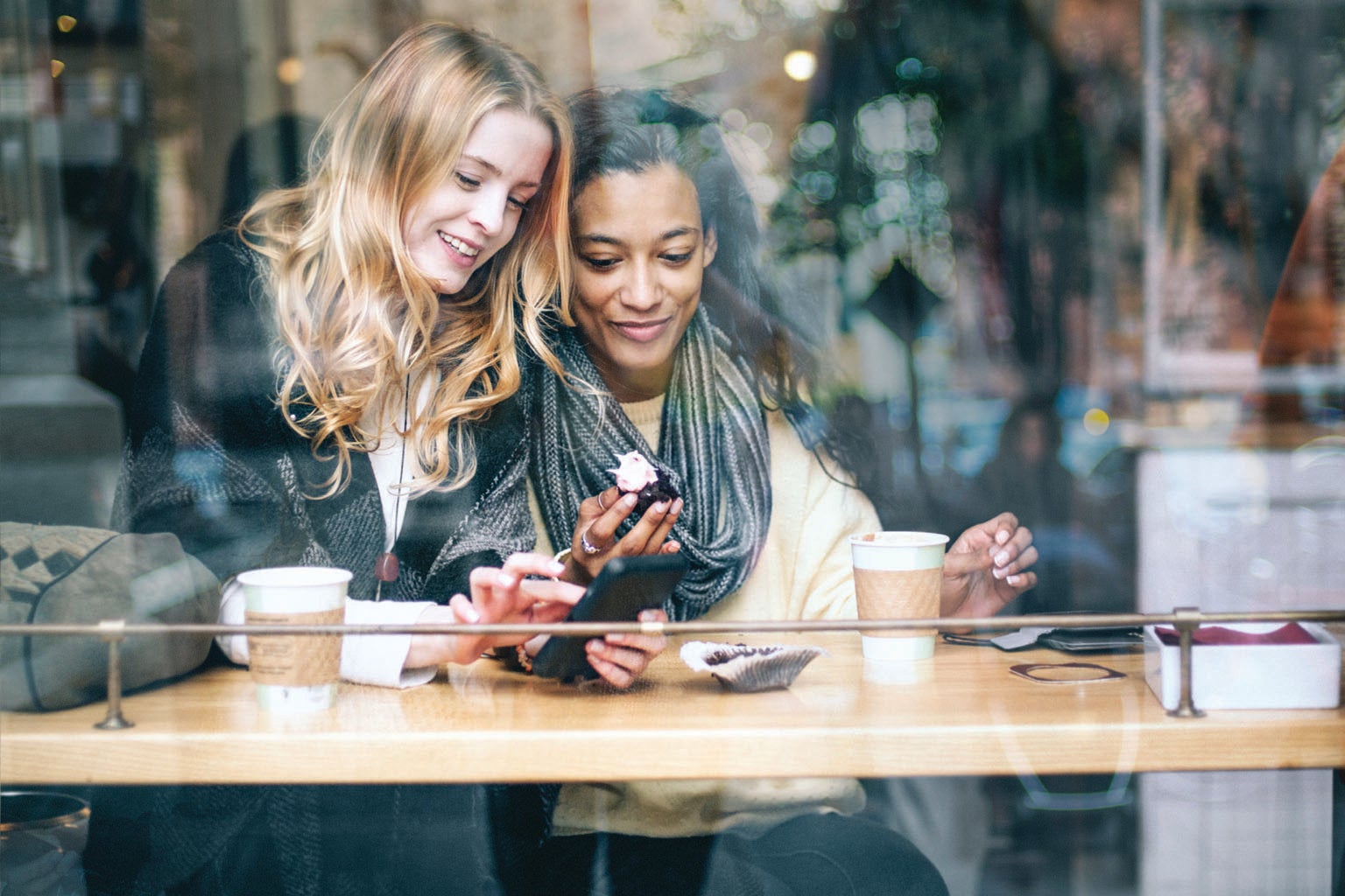 Two friends smiling as they look at a smartphone.