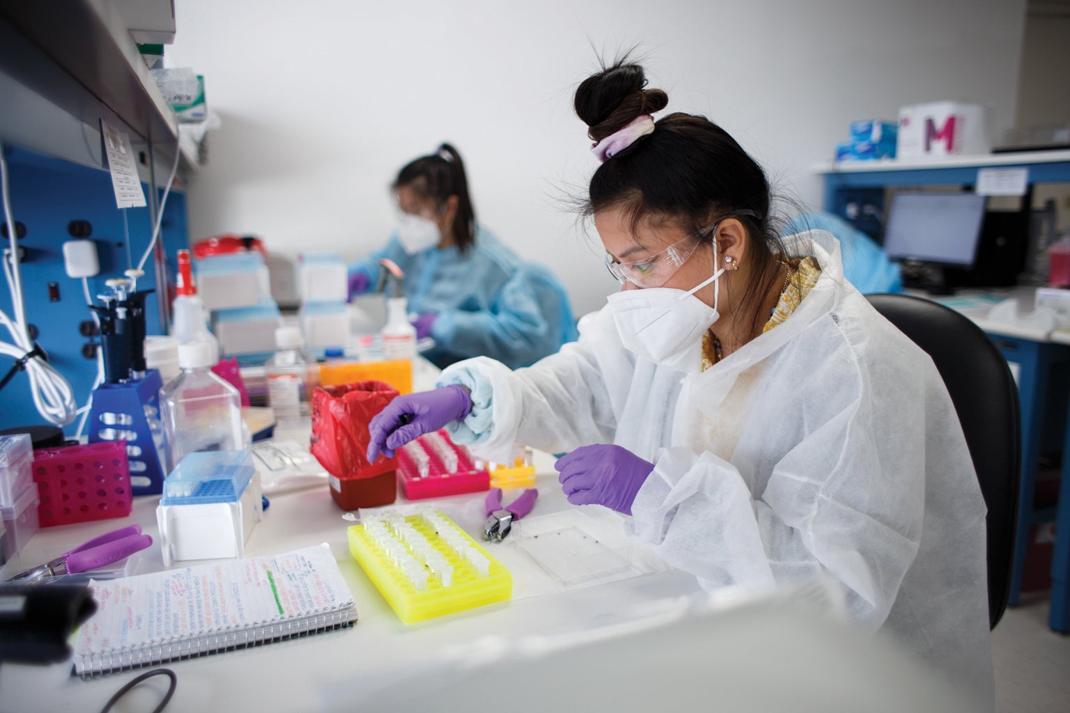 Two people working at a lab in front of a table full of testing tubes.