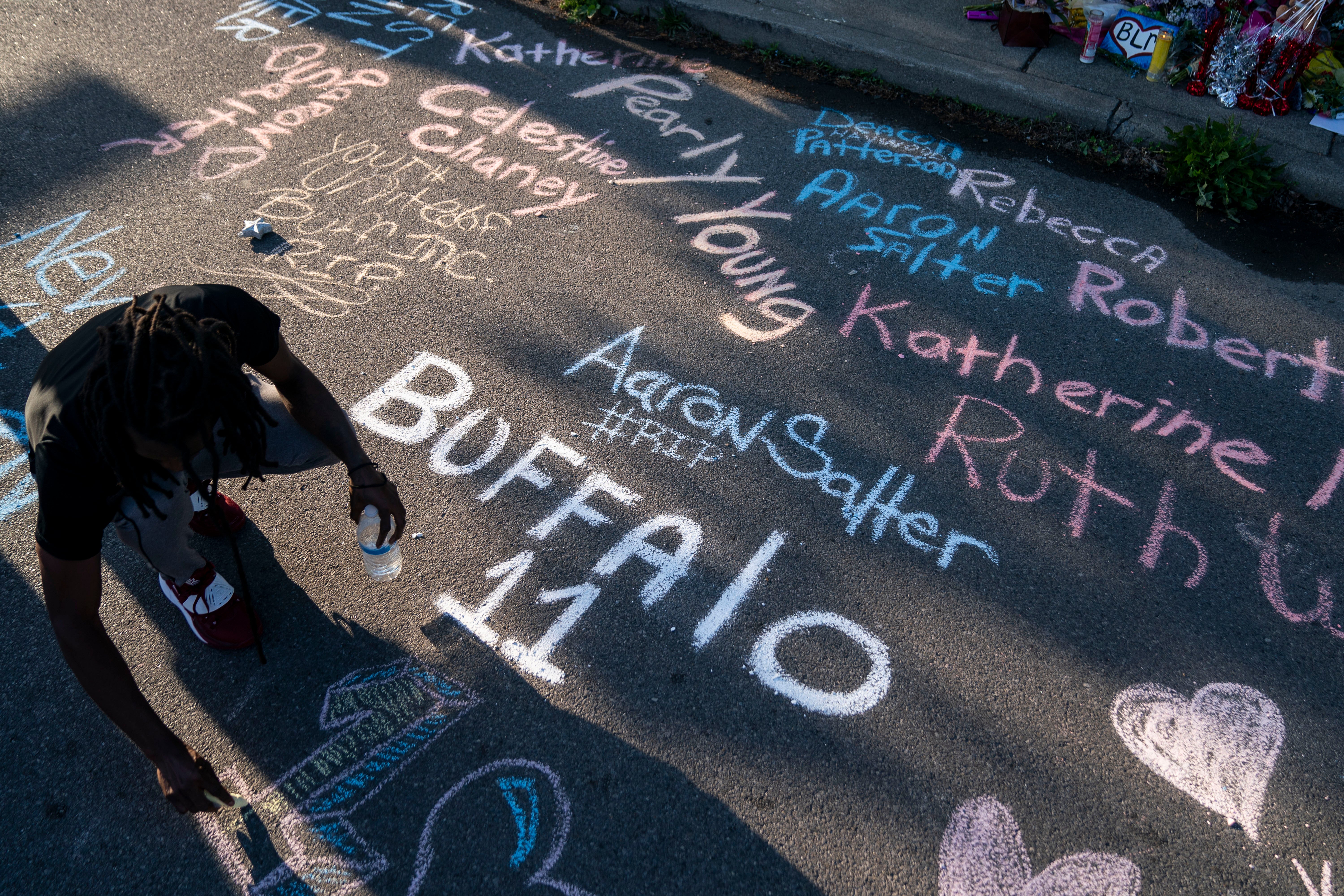 Shadow of a man adding names from the Buffalo shooting to a sidewalk chalk mural.