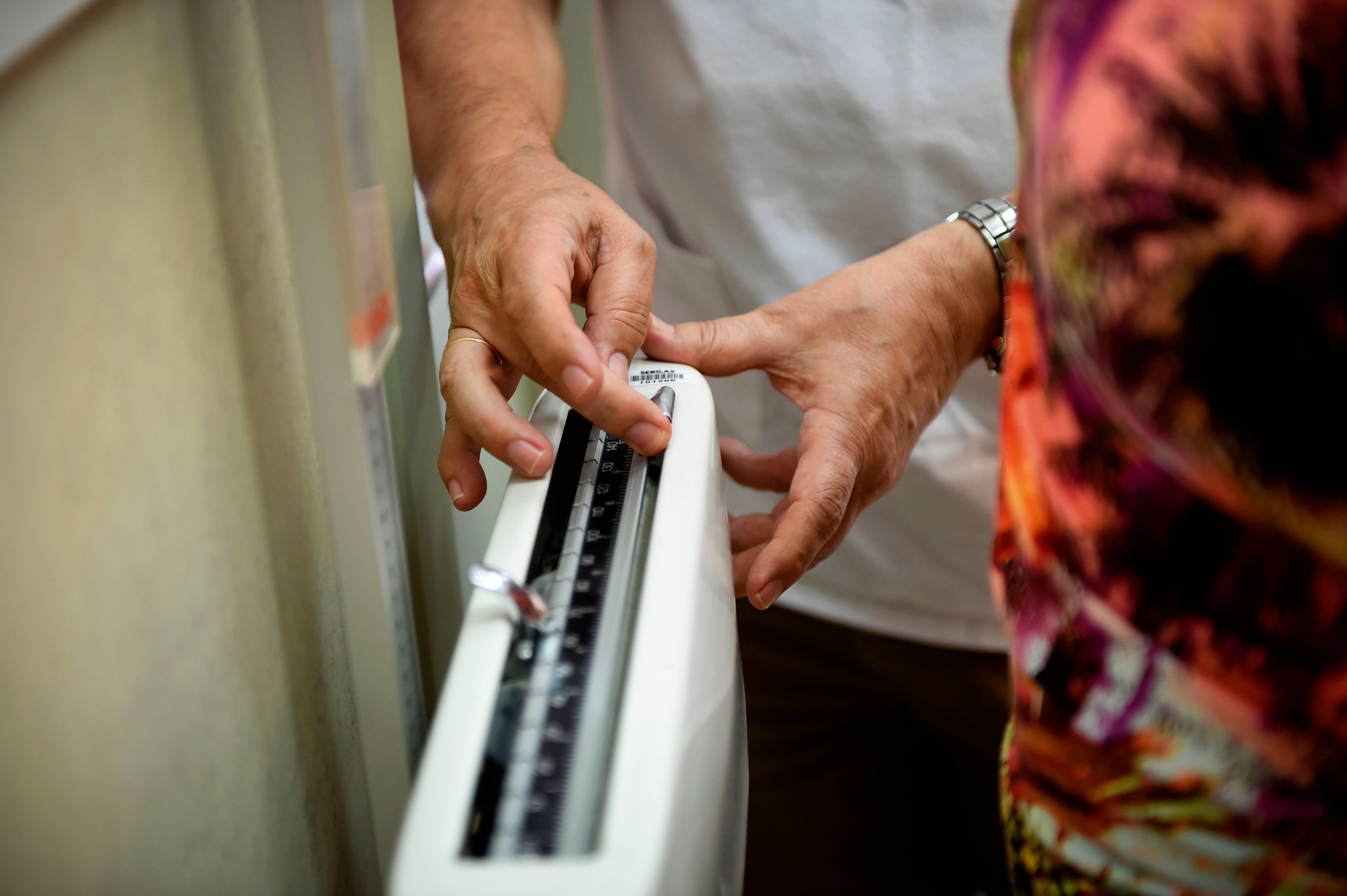 Mid section of a woman on a scale being weighed by a doctor 