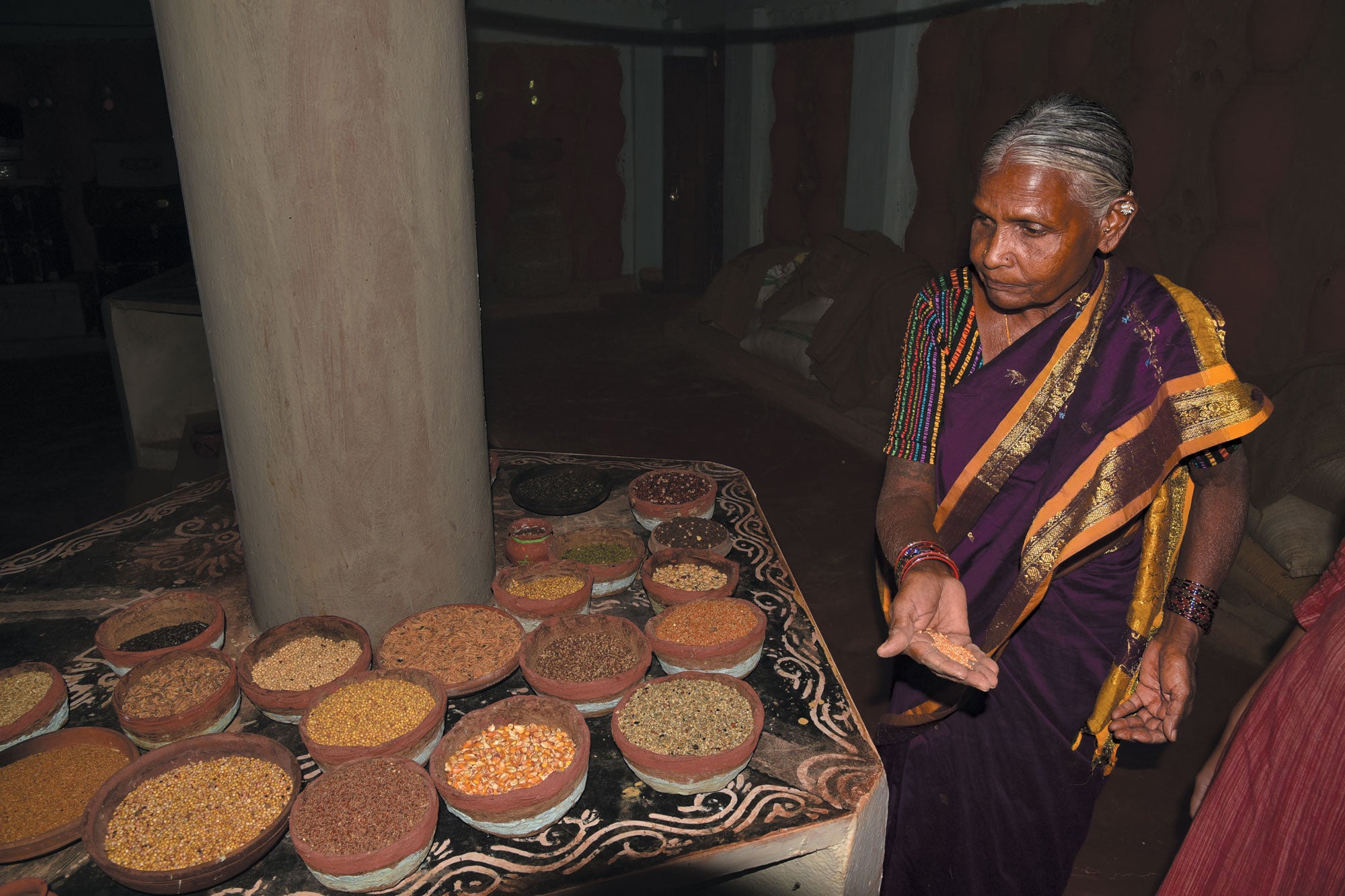 Woman showing handful of seeds selected from one of the containers on the table in front of here.