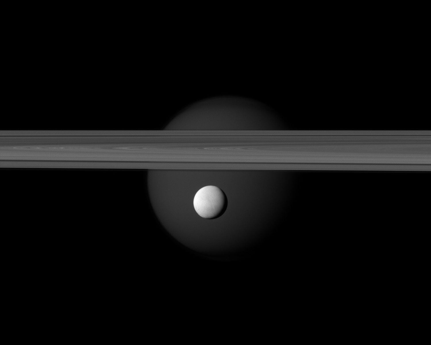 A brightly reflective Enceladus appears before Saturn's rings, while the planet's larger moon Titan looms in the distance