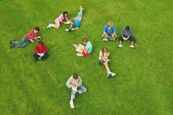Adolescents reading books on green grass.