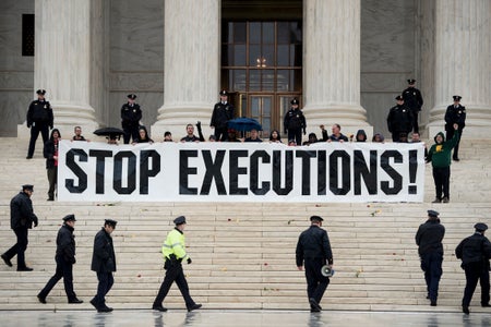 Police officers approach a crowd sitting that is holding a sign that reads "Stop Executions" that is sitting in the front of the Supreme Court building