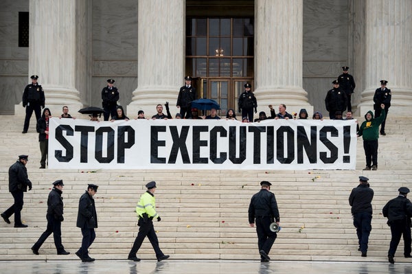 Police officers approach a crowd sitting that is holding a sign that reads "Stop Executions" that is sitting in the front of the Supreme Court building